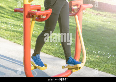 Young woman training with exercise equipment in a public park. In the background green grass with white flowers. The concept of maintaining a slim fig Stock Photo