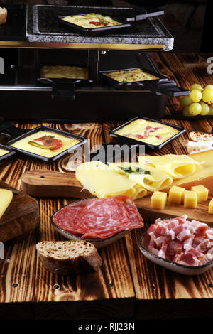 Delicious traditional Swiss melted raclette cheese served in individual skillets with salami Stock Photo