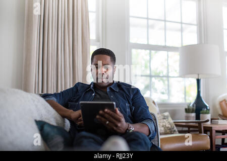 African American adult male using digital tablet at home on sofa Stock Photo