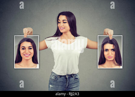 Young cheerful woman holding pictures with good and bad emotions having mood swings and smiling at positive herself Stock Photo