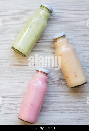 Fruit smoothies of different colors in glass bottles on white wooden surface. Top view, from above. Stock Photo
