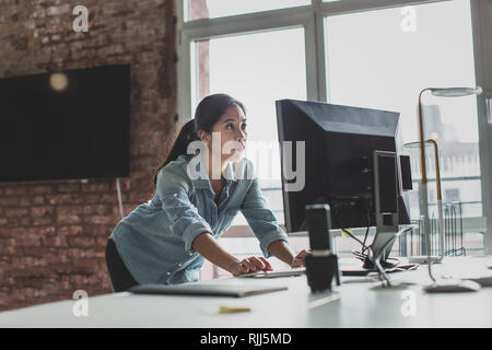 Young adult female standing and working on a desktop computer Stock Photo