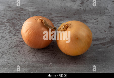 Side view of two whole yellow onions on a gray marble counter top. Stock Photo