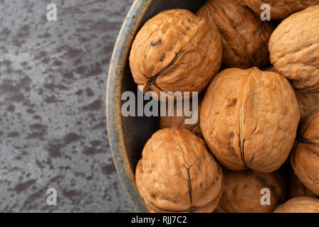 Top close view of an old stoneware bowl filled with walnuts on a gray counter top illuminated with natural lighting. Stock Photo