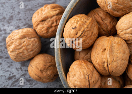 Overhead close view of an old stoneware bowl filled with walnuts plus three nuts to the side on a gray counter top. Stock Photo