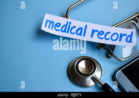 Conceptual image with Medical record inscription with the view of stethoscope, eyeglasses and smartphone on the blue background. Medical Conceptual. Stock Photo