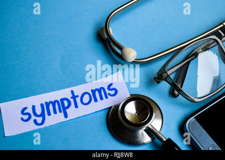 Conceptual image with Symptoms inscription with the view of stethoscope, eyeglasses and smartphone on the blue background. Medical Conceptual. Stock Photo