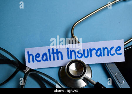 Conceptual image with Health insurance inscription with the view of stethoscope, eyeglasses and smartphone on the blue background. Medical Conceptual. Stock Photo