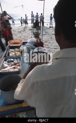 Caption: Fort Cochin, Kerala, India - May 2003. A snack vendor roasts peanuts as he waits for customers on the beach at Fort Cochin, the touristy Port Stock Photo