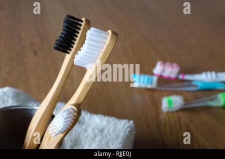 Three Bamboo toothbrushes against three plastic toothbrushes on wooden background Stock Photo