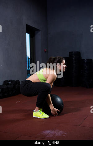 Theme sport and health. A strong muscular Caucasian woman in the gym trains strength and endurance. Equipping a large printed black ball raises and Stock Photo