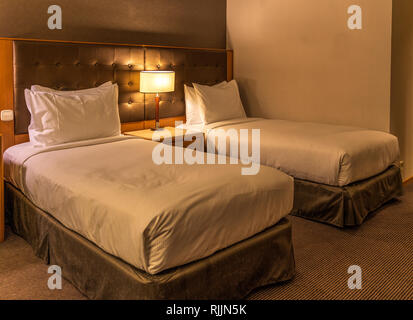 Two beds and common headrest with table lamp in a standard hotel room Stock Photo