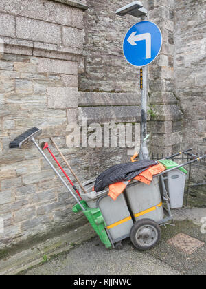 Street cleaner's trolley cart pulled up beside Turn Left road sign. Stock Photo