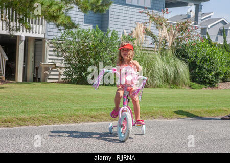 Little girl learning to ride a bike with training wheels. Stock Photo