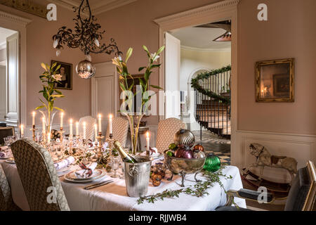 Mercury candlesticks on mantelpiece with lilies below decorative late 19th century copper chandelier. Stock Photo