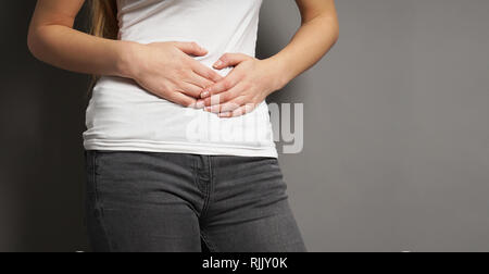 unrecognizable young woman holding her stomach with both hands - concept for dysmenorrhea, abdominal pain, bellyache, stomachache, painful periods or Stock Photo