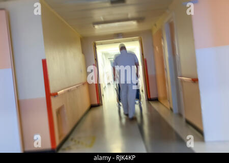 in a large and long corridor male nurse phushing an handicaped persone Stock Photo