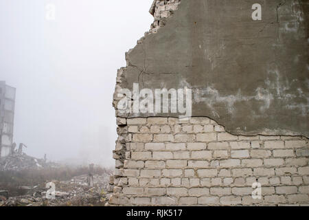 The remains of the destroyed wall of the building silicate white brick with partially peeling gray plaster solution. Stock Photo