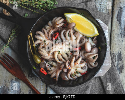 Baby octopus cooked, roasted in the iron pan portion, with lemon and seasoning close up Stock Photo