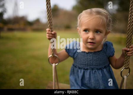 Happy little girl swings on a rope swing in the garden. Stock Photo