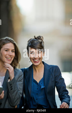 Two laughing young woman chat happily while walking home from the office. Stock Photo
