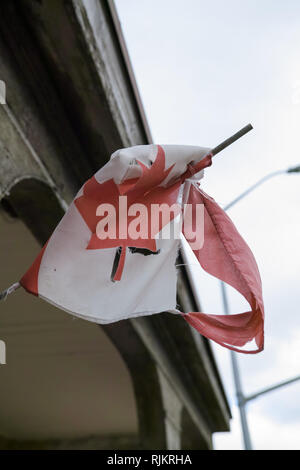 A worn-out and torn small Canadian flag, hanging sadly on the side of a historic building. Stock Photo