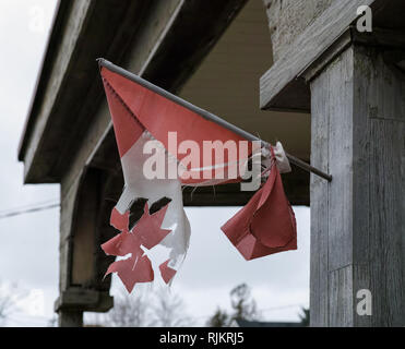 A worn-out and torn small Canadian flag, hanging sadly on the side of a historic building. Stock Photo