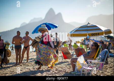 RIO DE JANEIRO - FEBRUARY, 2018:  A beach vendor selling brightly patterned canga sarongs and hats walks displaying his merchandise on Ipanema Beach. Stock Photo