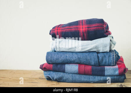 Jeans and plaid red shirts stacked on a wooden table. Hipster denim textiles clothing background pile concept. Copy space. Stock Photo