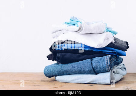 Stack of clothes on table indoor. Household concept. Fresh folded cotton jeans clothing. Ironing, donation, housework concept. Stock Photo
