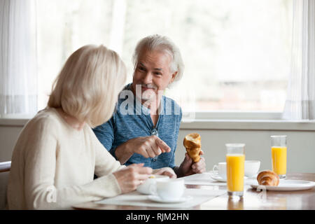 Positive aged spouses eating breakfast talking sitting in the kitchen Stock Photo