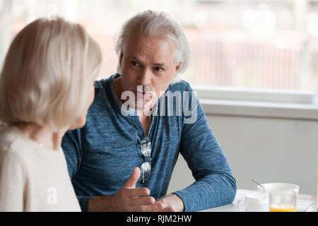 Senior spouses talking sitting together at table focus on husband Stock Photo
