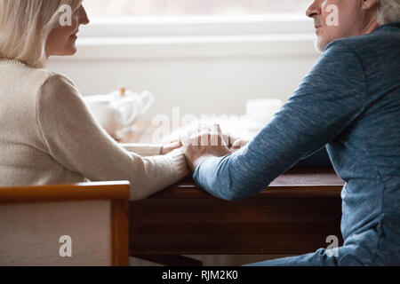 Cropped image middle aged couple sitting at table holding hands Stock Photo