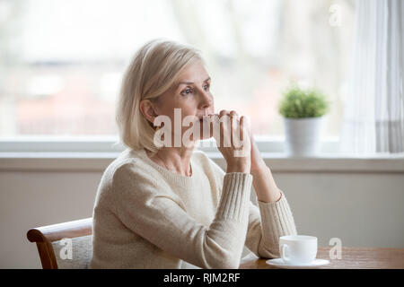 Thoughtful woman sitting at table with cup of tea  Stock Photo