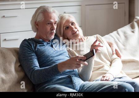 Surprised souses sitting on couch watching tv Stock Photo