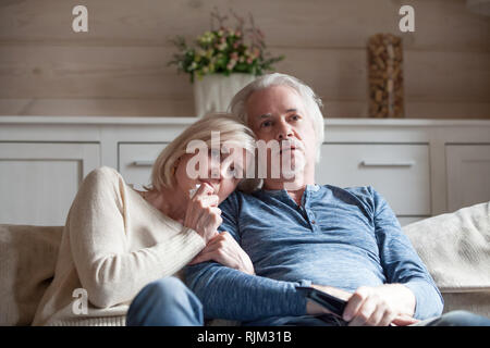 Old age spouses sitting on couch watching thriller movie Stock Photo