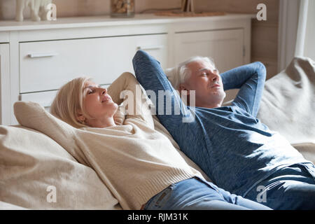 Aged spouses lying on couch putting hands behind head Stock Photo