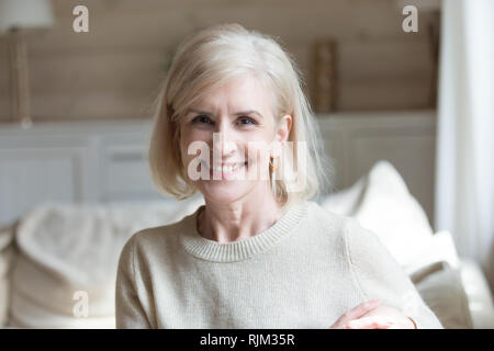 Smiling aged female sitting in living room looking at camera Stock Photo