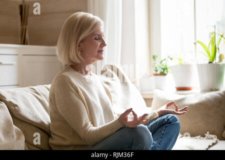 Focused senior woman doing yoga at home. 70 years old woman sitting on  fitness mat with outstretched hands resting on her knees performing yoga in  liv Stock Photo - Alamy