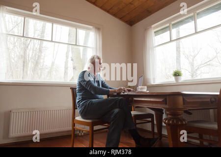 Senior man sitting at desk working on computer Stock Photo