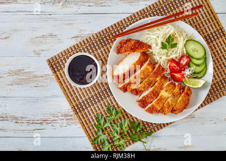 Tonkatsu - panko breaded deep-fried pork cutlet served with fresh shredded cabbage salad, tomatoes and lime slices on a plate on a bamboo mat, Japanes Stock Photo