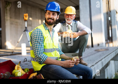 Happy young and senior engineer worker sitting at building site on break Stock Photo