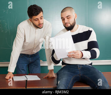 Portrait of two young guys discussing their student project at desk in classroom Stock Photo