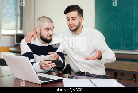 Male university students using their mobile phone instead of studying at classroom Stock Photo