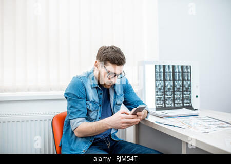 Man using smartphone sitting hunched down having scoliosis in the office of therapist at the clinic Stock Photo