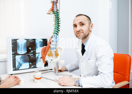 Portrait of a senior therapist sitting with anatomical model of the human spine in the medical office Stock Photo