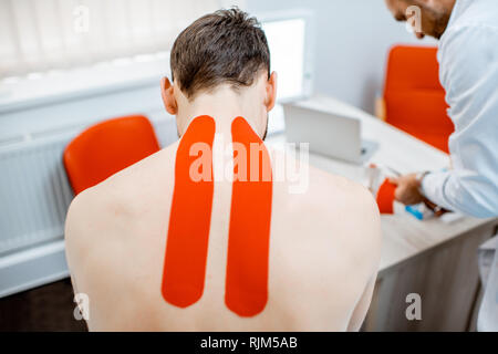 Man's neck with red kinesio tapes in the therapist office