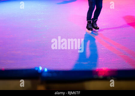 Closeup of human legs in old skates on outdoor public ice rink. Young figure skating on frozen lake in snowy winter park at night Stock Photo