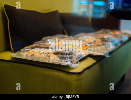 Take away Asian food on the plates wrapped in plastic bag on the couch Stock Photo
