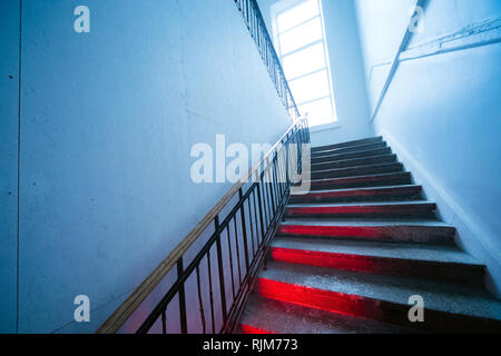 Looking up the scary distorted stairway. Stairs going up with red light on steps Stock Photo